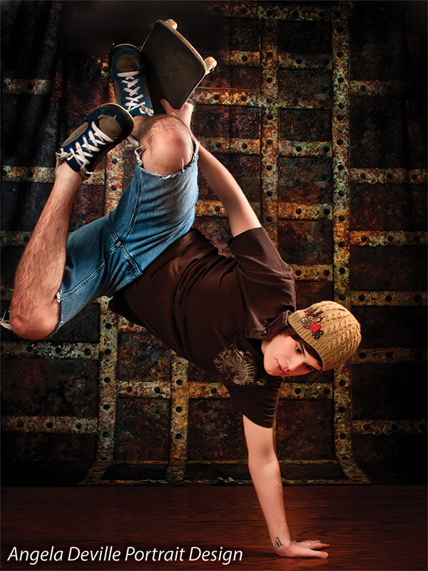Breakdancer with skateboard performing in front of a rusted steel grid backdrop, ideal for dynamic dance and street-style shoots.